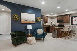 Kitchen featuring black appliances, light colored carpet, a breakfast bar area, a peninsula, and dark countertops