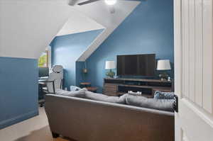 Living room with carpet, ceiling fan, vaulted ceiling, baseboards, and a desk