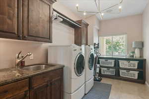 Washroom featuring washing machine and clothes dryer, cabinet space, light tile patterned floors, and a chandelier