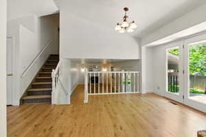 Unfurnished living room featuring a chandelier, wood finished floors, high vaulted ceiling, baseboards, and stairway