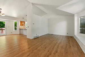 Unfurnished living room featuring lofted ceiling, light wood-type flooring, and baseboards
