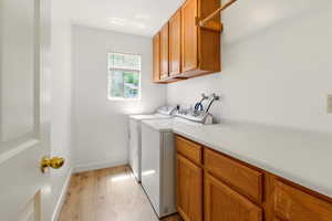 Laundry room featuring cabinet space, light wood-style flooring, independent washer and dryer, and baseboards