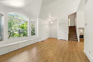 Unfurnished living room with vaulted ceiling, light wood-style flooring, plenty of natural light, stairway, and baseboards