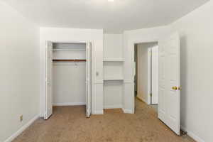 Unfurnished bedroom with light carpet, a closet, and baseboards