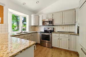 Kitchen featuring appliances with stainless steel finishes, a sink, lofted ceiling, light wood-type flooring, and light stone countertops