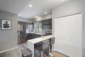 Kitchen with stainless steel appliances, a peninsula, light wood-style flooring, light countertops, and a breakfast bar area