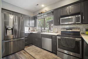 Kitchen with stainless steel appliances, light countertops, a sink, wood finished floors, and decorative backsplash