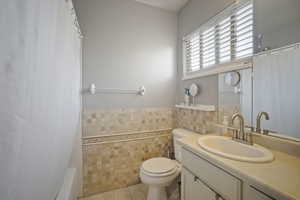 Bathroom with vanity, toilet, tile patterned floors, shower / bath combination with curtain, and tile walls