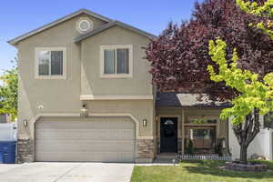 View of front of house with stone siding, driveway, a garage, and stucco siding