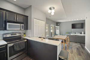 Kitchen featuring stainless steel appliances, a peninsula, wood finished floors, light countertops, and backsplash