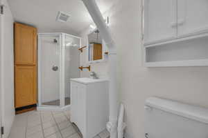 Bathroom with a shower stall, toilet, vanity, tile patterned flooring, and tile walls