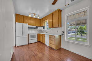 Kitchen featuring white appliances, under cabinet range hood, dark wood-style floors, baseboards, and light countertops