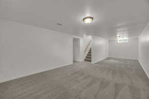 Basement featuring stairway, light carpet, and baseboards