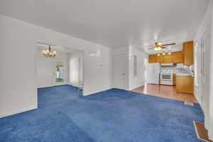 Unfurnished living room featuring carpet flooring, a ceiling fan, a chandelier, and baseboards