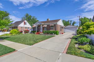 Bungalow-style house featuring brick siding, an outbuilding, a detached garage, a chimney, and a front yard