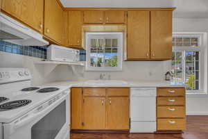 Kitchen with white appliances, a sink, under cabinet range hood, and light countertops