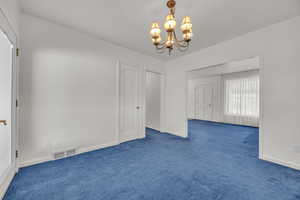 Empty room with carpet floors, a chandelier, and baseboards