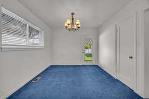 Unfurnished room with a chandelier, dark colored carpet, and baseboards