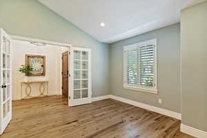 Formal front room or office with french doors, wood floors, lofted ceiling, plantation shutters and recessed lighting