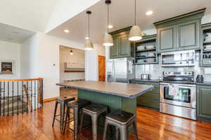 Kitchen featuring stainless steel appliances, green cabinetry, open shelves, and recessed lighting