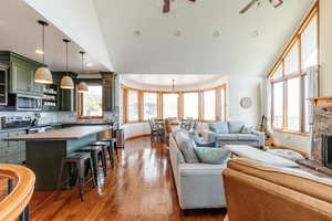 Living room featuring ceiling fan, baseboards, high vaulted ceiling, dark wood finished floors, and a stone fireplace