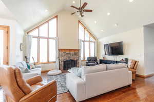 Living room featuring a stone fireplace, ceiling fan, hardwood / wood-style floors, baseboards, and high vaulted ceiling