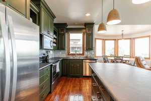 Kitchen featuring appliances with stainless steel finishes, green cabinetry, dark wood-style flooring, tasteful backsplash, and a sink