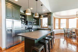 Kitchen featuring stainless steel appliances, green cabinets, open shelves, dark countertops, and baseboards