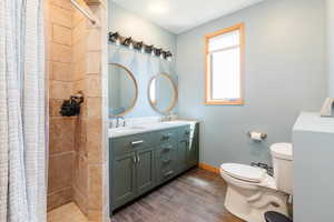 Full bath featuring toilet, double vanity, tiled shower, and wood finish floors
