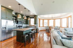 Kitchen with green cabinetry, stainless steel appliances, open shelves, open floor plan, and dark countertops
