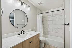 Full bath with updated vanity, toilet, shower / bath combination with curtain, and tile pattern