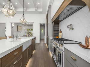 Kitchen featuring double oven range, a sink, dark wood finished floors, light stone counters, and decorative light fixtures