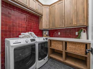 Laundry area with cabinet space, washing machine and dryer, and dark tile patterned flooring