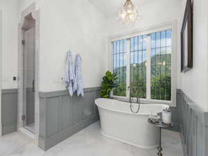 Bathroom featuring marble tiled flooring, a wainscoted wall, a stall shower, a freestanding tub, and a chandelier
