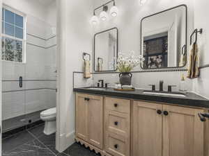 Bathroom featuring marble finish floors, toilet, a stall shower, and double vanity