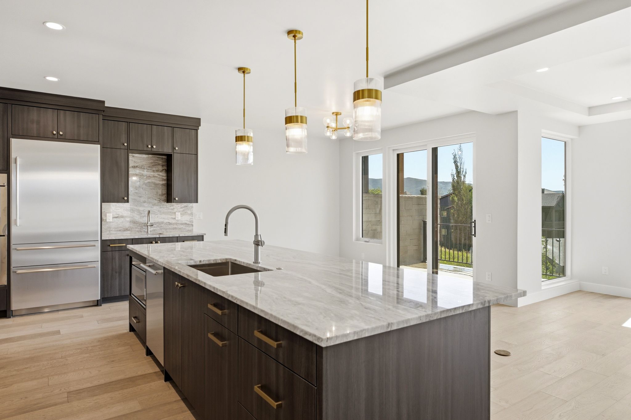 Kitchen featuring a large island with an undermount sink and a light-toned countertop, dark wood-finish cabinetry, stainless steel appliances, and wood-finish flooring