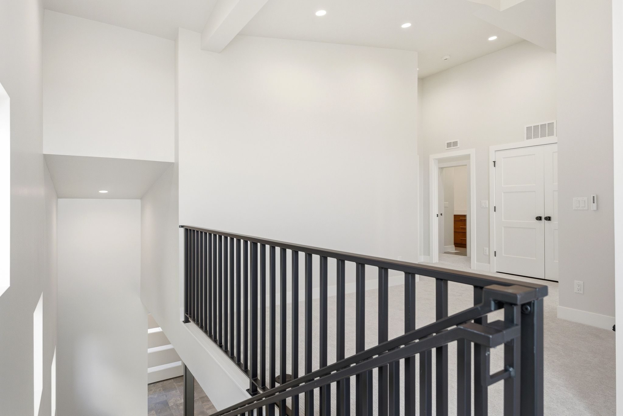 Modern interior featuring a black metal railing, high ceilings, recessed lighting, and light gray carpet