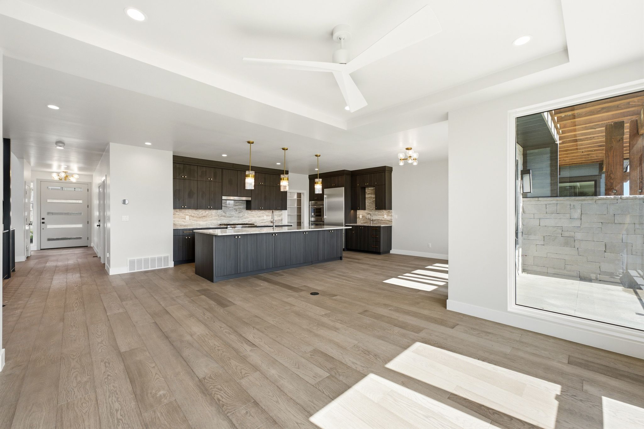 Open-concept living area featuring wide-plank wood-finish flooring, a contemporary kitchen with dark cabinetry, a large kitchen island with pendant lighting, a stainless steel refrigerator, and recessed lighting