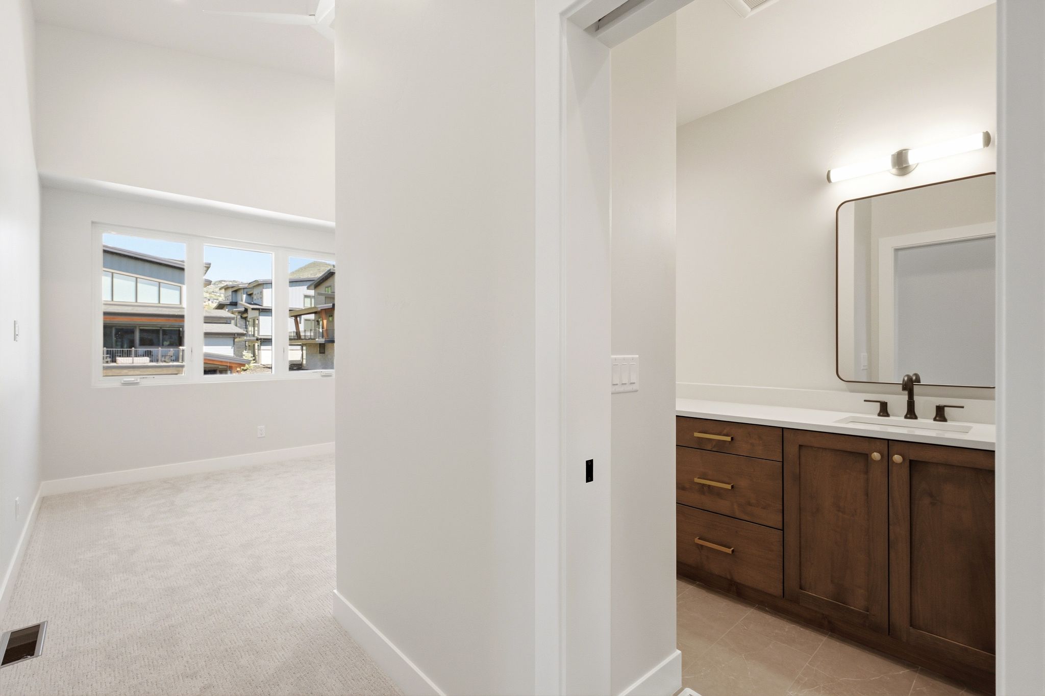 Modern vanity area featuring a rectangular mirror, sconce lighting, a single basin sink, wood cabinetry, and light-toned countertops