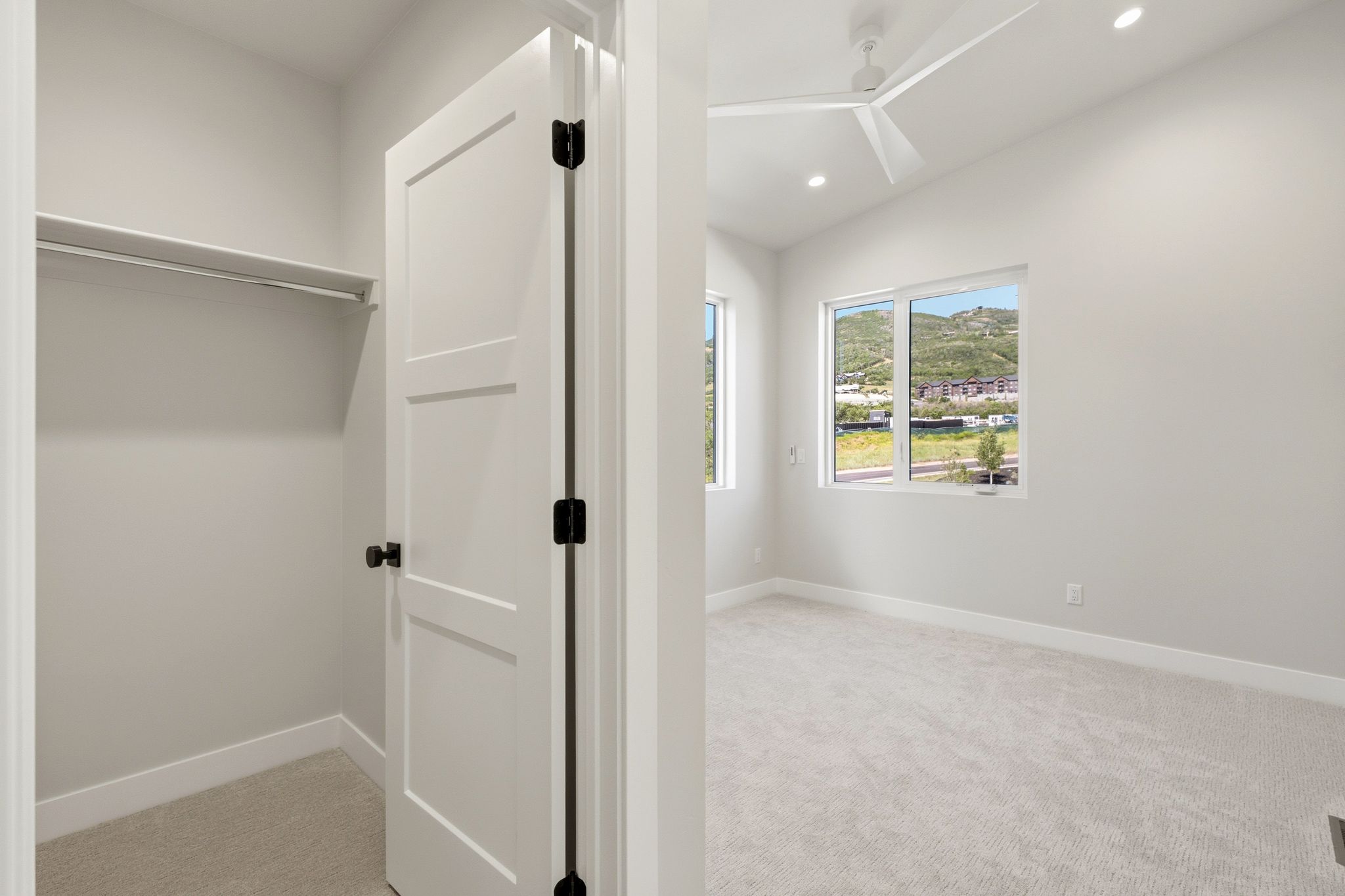 Bright room featuring a contemporary ceiling fan, recessed lighting, and two windows showcasing distant hills