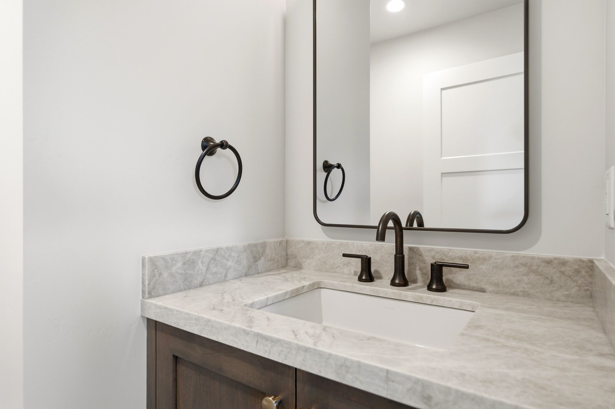 Vanity featuring an integrated sink, stone countertop, dark wood-finish cabinetry, and matte black hardware