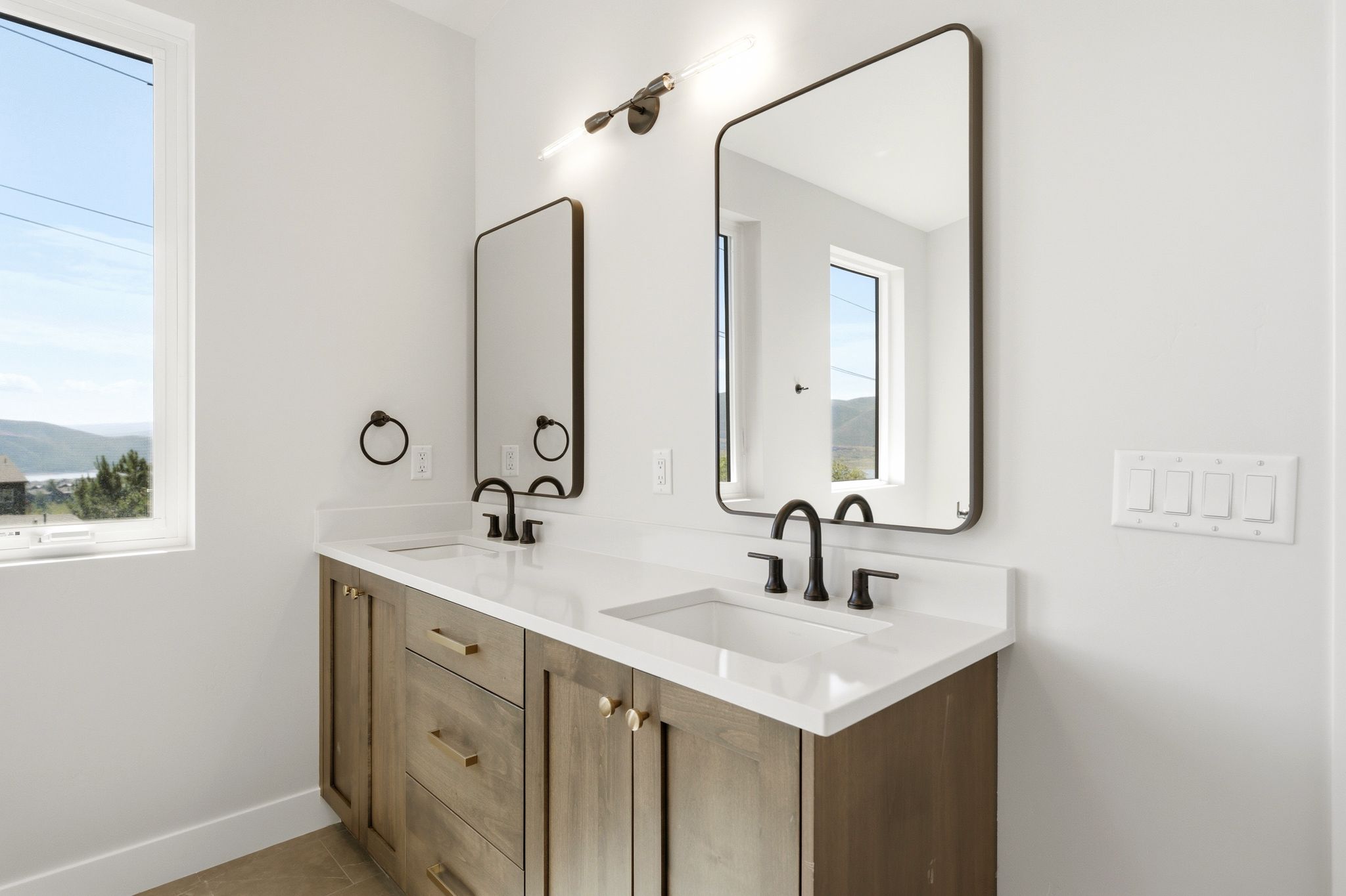 Contemporary double vanity with light wood-finish cabinetry, white countertops, and integrated rectangular sinks