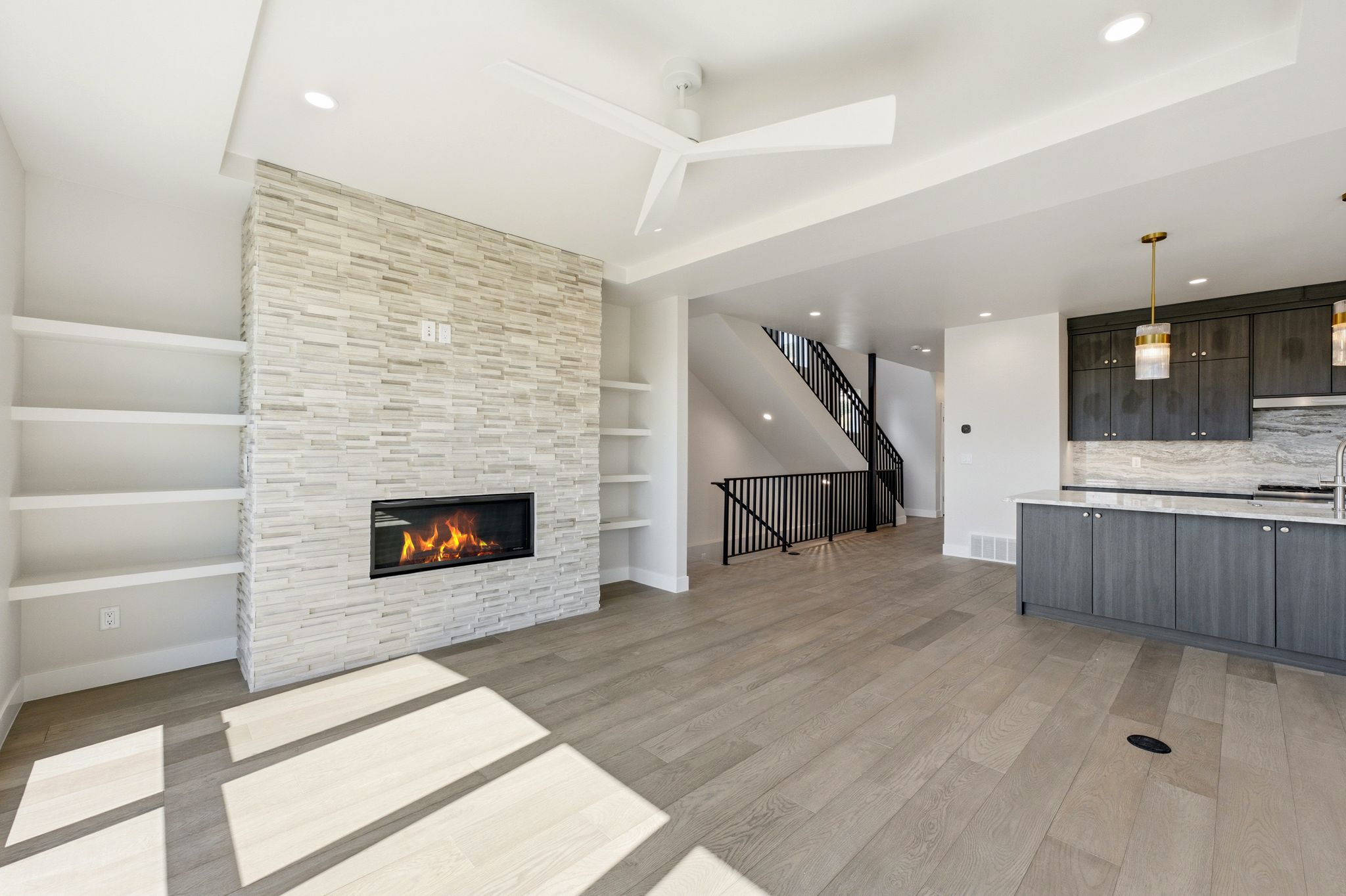Open-concept living area featuring wood-finish flooring, a contemporary fireplace with a stacked stone surround, and integrated shelving
