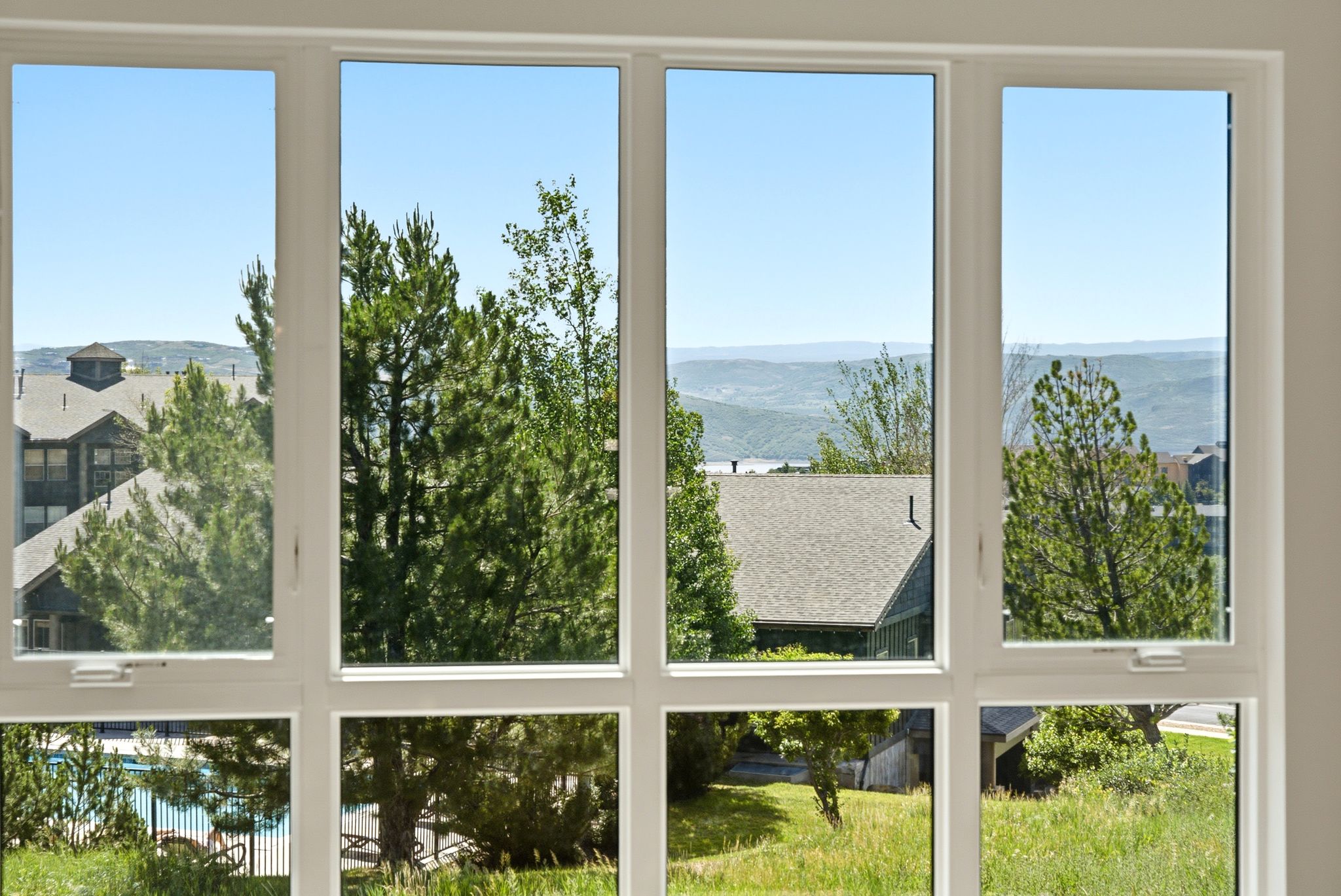 Expansive multi-pane window framing a landscape with distant mountains, lush trees, and surrounding rooftops
