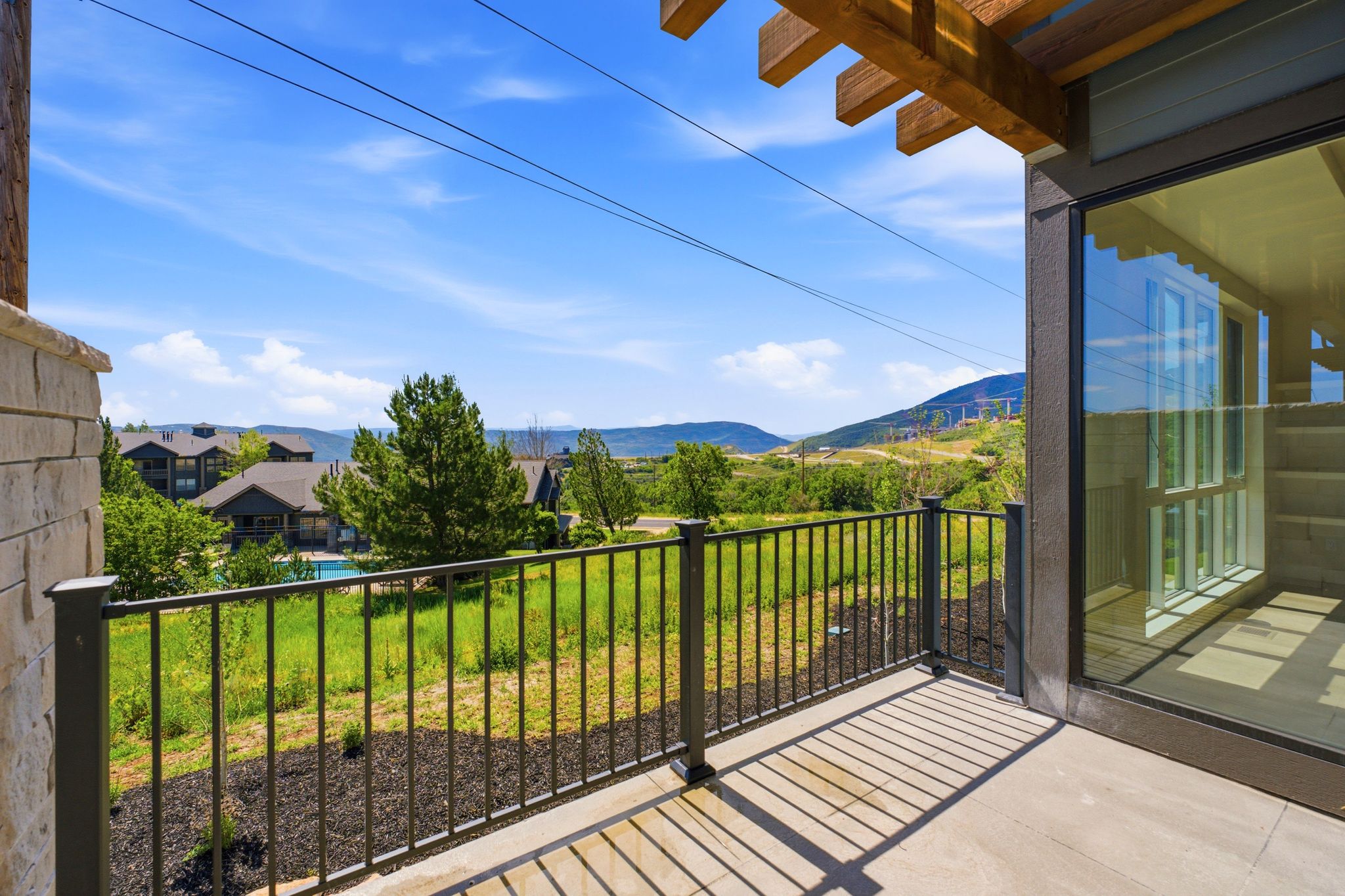 Outdoor balcony featuring a wood pergola, stone column, and black metal railing