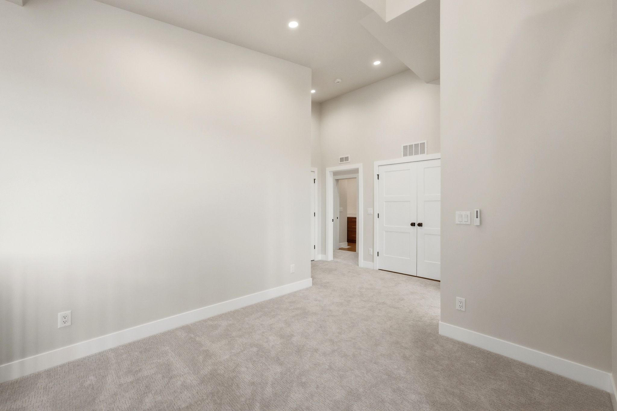 Spacious room featuring vaulted ceilings, recessed lighting, light gray carpet, white trim, and white double doors