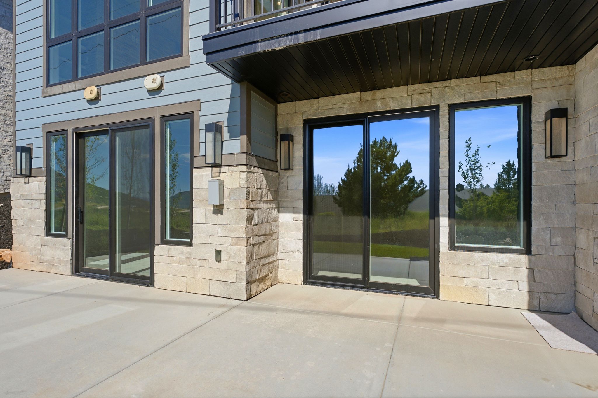 Outdoor patio featuring a concrete surface, stone veneer siding, light blue horizontal siding, multiple sliding glass doors, and contemporary exterior lighting fixtures