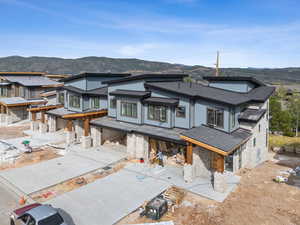 Rear view of property featuring stone siding, roof with shingles, a patio area, and a mountain view