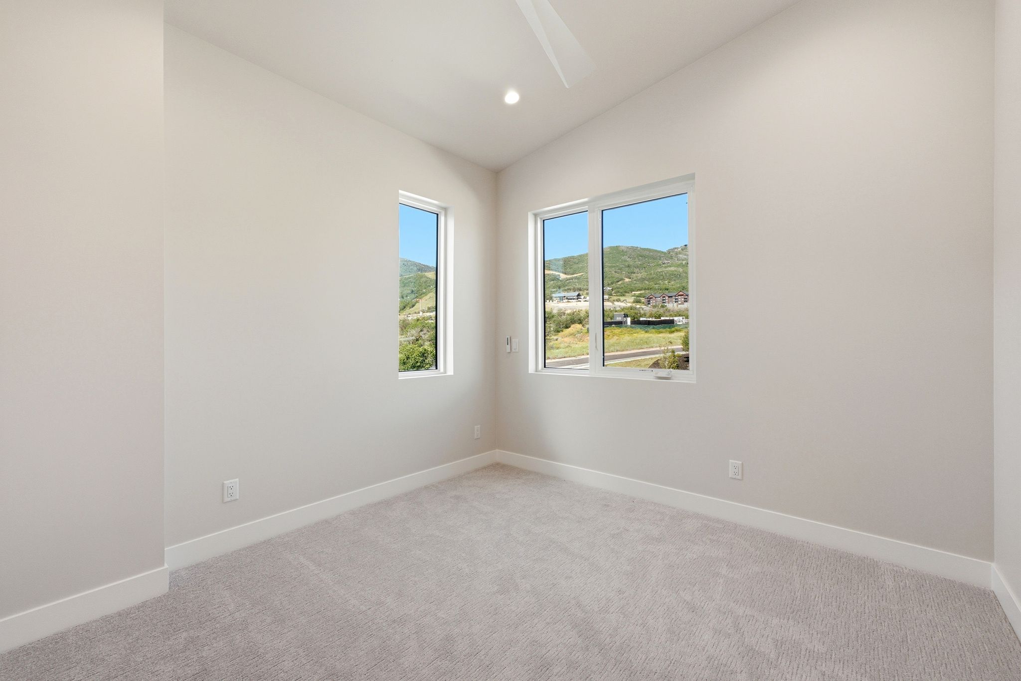 Bright room featuring two windows, neutral carpeting, white trim, recessed lighting, and a ceiling fan