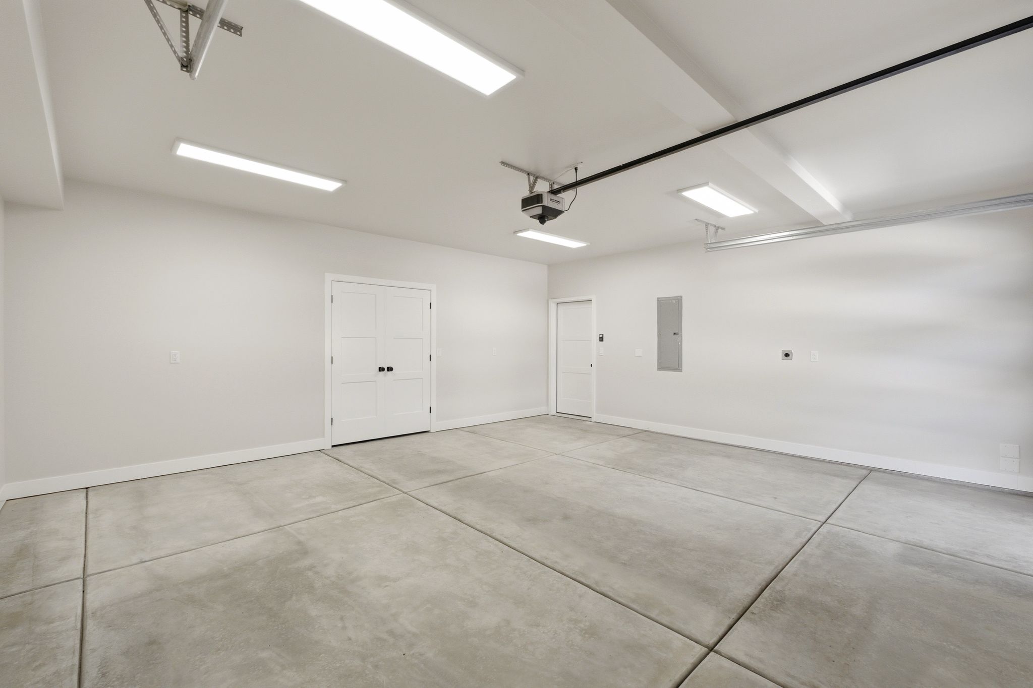 Spacious garage featuring a concrete floor, multiple ceiling-mounted lighting fixtures, a double-panel interior door, and an additional single interior door
